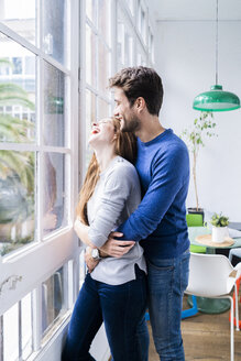 Glückliches, zärtliches Paar, das sich am Fenster zu Hause umarmt - GIOF06495