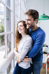 Glückliches, zärtliches Paar, das sich am Fenster zu Hause umarmt - GIOF06496
