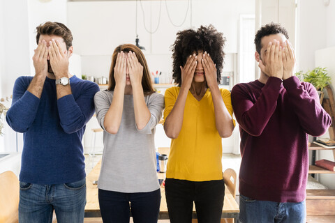Four friends standing side by side at home covering their faces stock photo