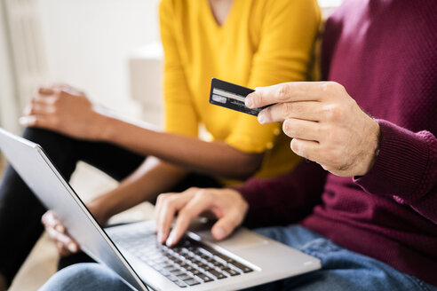 Nahaufnahme eines Paares, das zu Hause mit Laptop und Kreditkarte online einkauft - GIOF06501