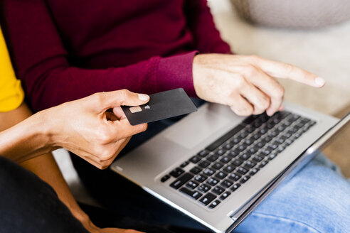 Nahaufnahme eines Paares, das zu Hause mit Laptop und Kreditkarte online einkauft - GIOF06503