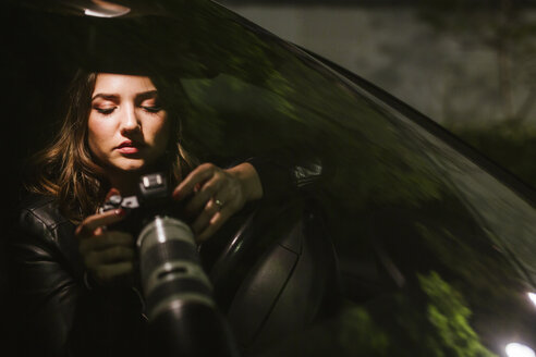 Junge Frau mit Kamera in einem Auto bei Nacht - LJF00108