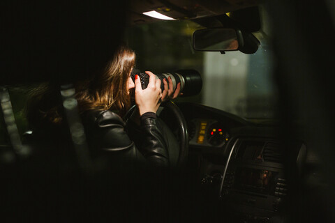 Junge Frau, die nachts aus einem Auto heraus Fotos mit einer Kamera macht, lizenzfreies Stockfoto