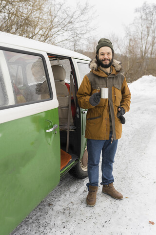 Porträt eines lächelnden Mannes mit einem elektrischen Lieferwagen in einer Winterlandschaft, Kuopio, Finnland, lizenzfreies Stockfoto