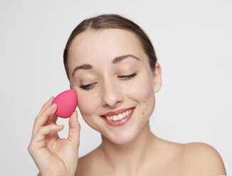 Porträt einer lächelnden jungen Frau mit rosa Make-up-Schwamm - PNEF01537