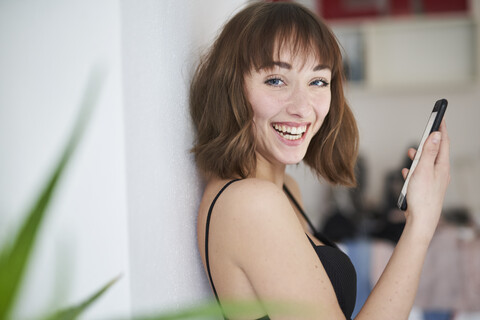 Porträt einer lachenden jungen Frau mit Smartphone zu Hause, lizenzfreies Stockfoto