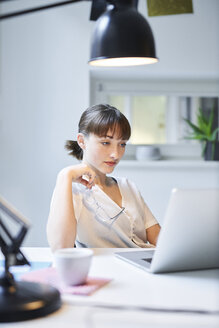 Porträt einer jungen Frau, die in einem Büro an einem Laptop arbeitet - PNEF01546