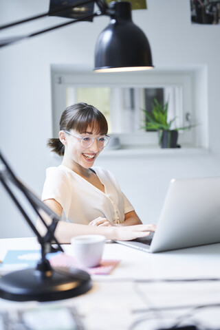 Portrait of laughing young woman working on laptop in an office stock photo