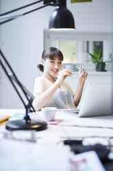 Portrait of smiling young businesswoman sitting at desk in an office - PNEF01549