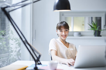 Portrait of smiling young woman working on laptop in an office - PNEF01550