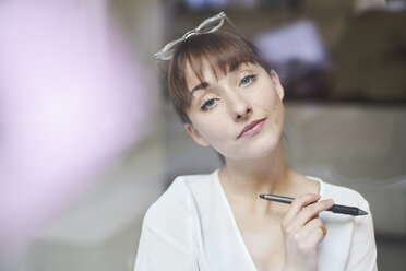 Porträt einer jungen Geschäftsfrau mit Brille und Bleistift hinter Glasscheibe - PNEF01553