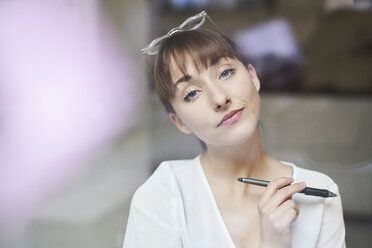 Portrait of young businesswoman with glasses and pencil behind glass pane - PNEF01553