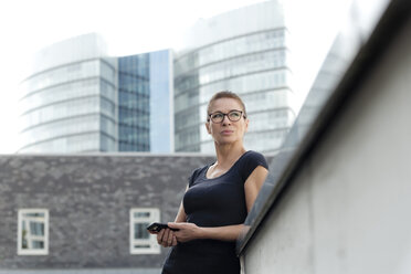 Frau mit Mobiltelefon vor einem Bürogebäude - FLLF00225