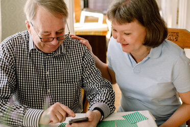Lächelnde reife Sozialarbeiterin, die einen älteren Mann im Ruhestand betrachtet, der ein Smartphone im Pflegeheim benutzt - MASF12364