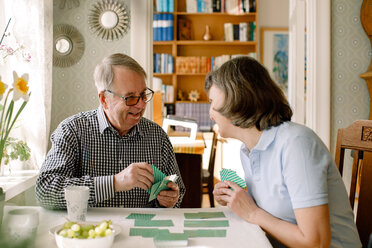 Lächelnder älterer Mann im Ruhestand, der mit einer reifen Krankenschwester am Tisch im Pflegeheim Karten spielt - MASF12365