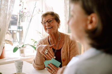 Lächelnde ältere Frau im Ruhestand schaut weg, während sie mit einer Sozialarbeiterin im Pflegeheim Karten spielt - MASF12372