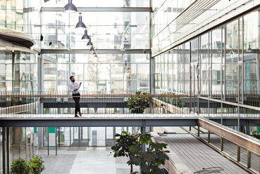 Junger Geschäftsmann in voller Länge im Atrium eines Büros stehend - MASF12376