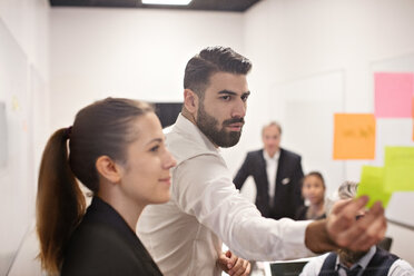 Young businessman explaining colleagues over adhesive notes in meeting at board room - MASF12399