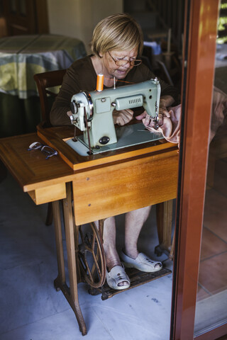 Ältere Frau benutzt eine alte Nähmaschine zu Hause, lizenzfreies Stockfoto