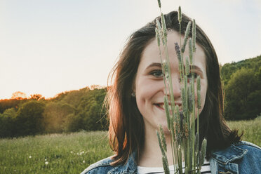 Porträt eines lächelnden Teenagers mit Gräsern bei Sonnenuntergang - ANHF00106