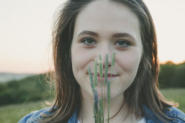 Porträt eines lächelnden Teenagers mit Gräsern bei Sonnenuntergang - ANHF00107