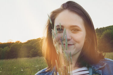 Porträt eines lächelnden Teenagers mit Gräsern bei Sonnenuntergang - ANHF00108