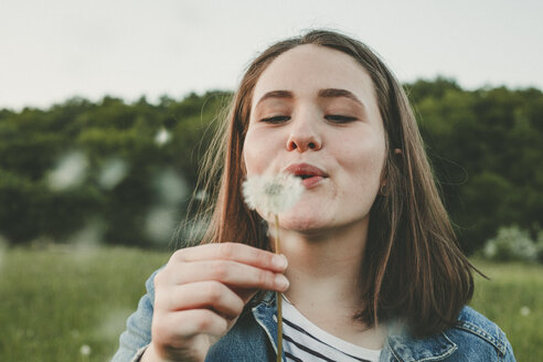 Portrait of teenage girl blowing blowball - ANHF00113