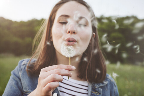 Porträt eines jugendlichen Mädchens, das einen Pusteball bläst, lizenzfreies Stockfoto