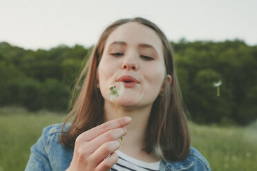 Portrait of teenage girl blowing blowball - ANHF00115