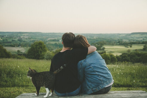 Back view of young lovers with cat enjoying nature at sunset - ANHF00118