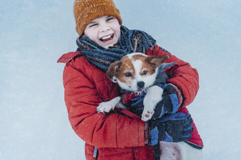Porträt eines lachenden Jungen und seines Hundes im Winter, lizenzfreies Stockfoto