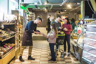 Store owner helping girl while couple discussing over mobile phone in supermarket - MASF12428