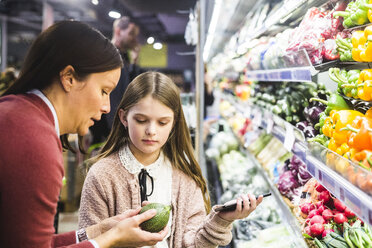 Mutter zeigt ihrer Tochter beim Einkaufen im Supermarkt eine Gurke - MASF12432