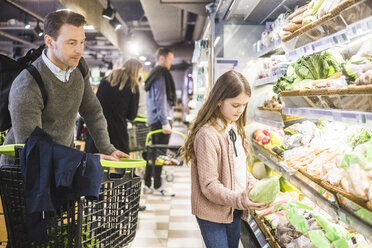 Vater schaut auf süße Tochter, die im Supermarkt Gemüse auswählt - MASF12436