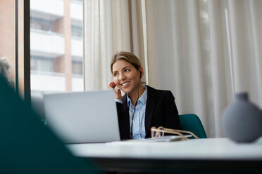 Smiling realtor talking through headphones while using laptop at estate office - MASF12480