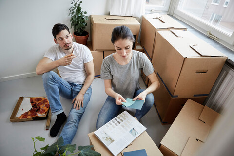 Nachdenkliches Paar mit Pizza und Farbmustern beim Umzug in ein neues Haus, lizenzfreies Stockfoto