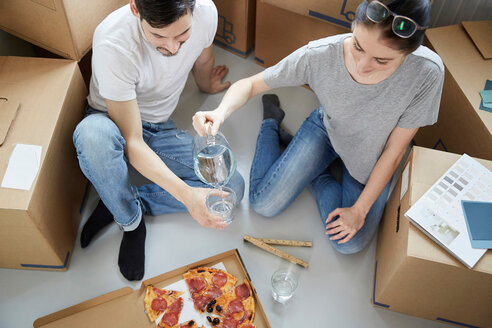 Eine Frau serviert einem Mann beim Pizzaessen während des Umzugs in ein neues Haus Wasser - MASF12502