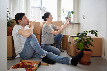 Man eating pizza while looking at woman choosing color swatches in new house - MASF12503