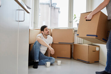 Mann mit Kaffeebechern schaut auf Frau, die Kartons in ein neues Haus trägt - MASF12510