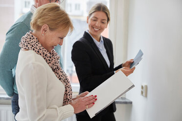 Smiling agent looking at senior couple with brochure deciding color samples for new house - MASF12513