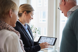 Eine Immobilienmaklerin zeigt einem älteren Ehepaar zu Hause den Bauplan eines neuen Hauses auf einem digitalen Tablet - MASF12535