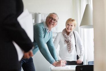 Smiling senior couple looking at real estate agent while signing for new house - MASF12538