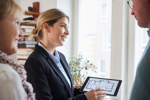 Ein lächelnder Immobilienmakler zeigt einem Paar auf einem digitalen Tablet den Bauplan eines neuen Hauses - MASF12539