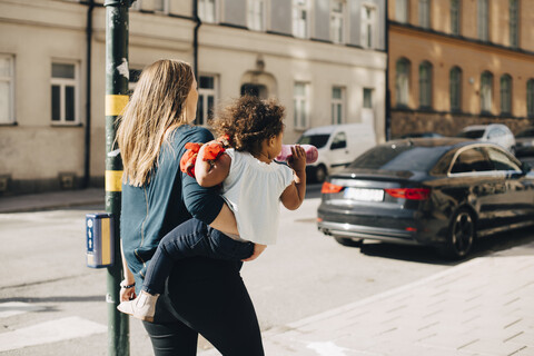 Mutter trägt ihre Tochter auf einem Fußweg in der Stadt, lizenzfreies Stockfoto