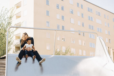 Mutter spielt mit ihrer Tochter auf einer Rutsche in einem Park in der Stadt - MASF12546