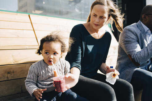 Frau sitzt mit Mann und füttert ihre Tochter mit einem Getränk, während sie im Park sitzt - MASF12547