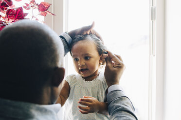 Rear view of father tying daughter's hair against window at home - MASF12552