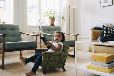 Full length of girl holding digital tablet while sitting on small armchair at home - MASF12555