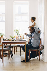 Father carrying daughter on shoulder while using laptop at table in house - MASF12559