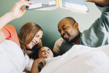 Glückliche Eltern, die ihrer Tochter ein Märchenbuch zeigen, während sie gemeinsam zu Hause im Bett schlafen - MASF12564